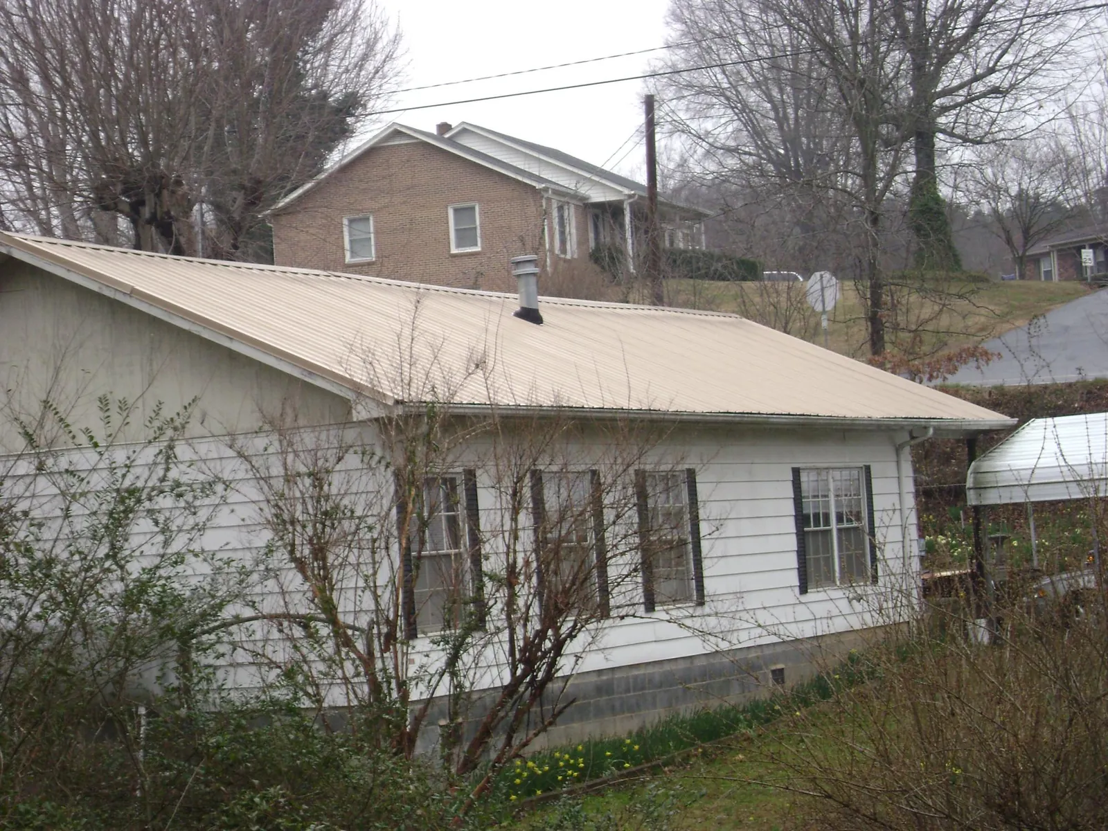Tan metal roof on a white sided house set into a hillside — Commercial Roofing by Roofing Brothers in Springbrook